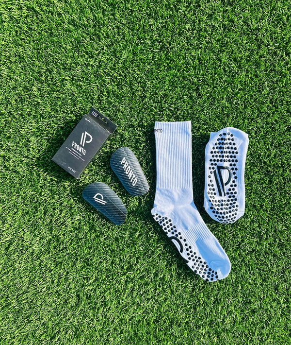 Pronto sæt med carbon shinguards, sokker og emballage på kunstgræs, alle med tydeligt 'PRONTO' logo.